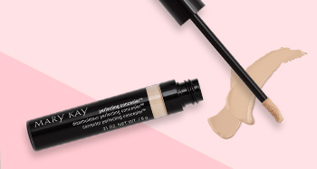 Otevřená tubička korektoru Mary Kay Perfecting Concealer vyfotografovaná společně s aplikátorem a ukázkou produktu před pozadím ve dvou odstínech růžové.