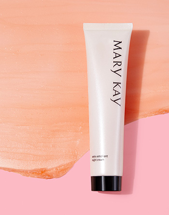 Detailní záběr na tubu Mary Kay® Extra zvláčňujícího nočního hydratačního krému pro suchou pleť na růžovém pozadí s ukázkou produktu.