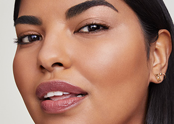 Mladá žena s hnědými rovnými vlasy dívající se přímo do kamery; usmívá se s pootevřenými ústy, její oči jsou rozzářené.