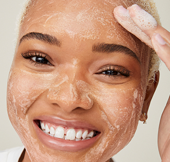 Usměvavá žena afrického původu provádí peeling s přípravkem Botanical Effects Povzbuzující peeling.